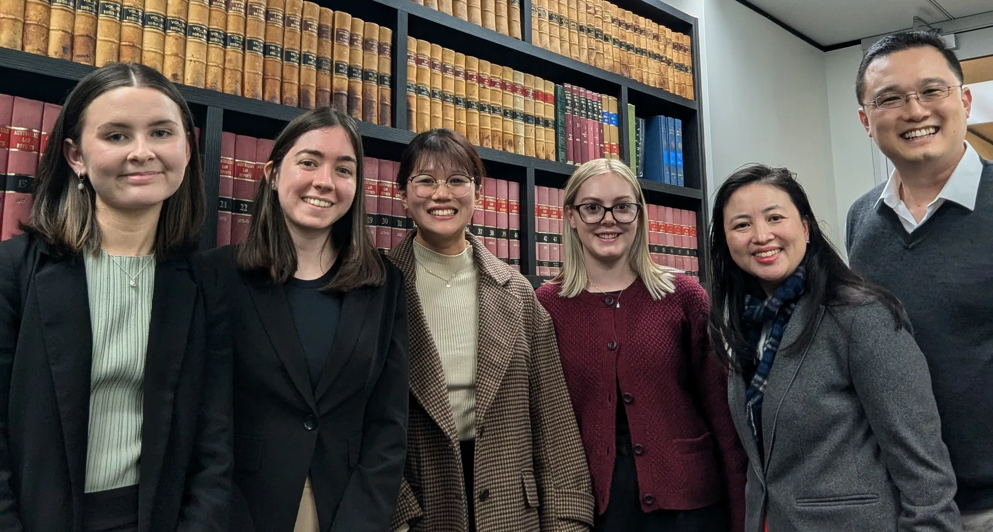 The YHC Lawyers team standing together in front of the office shelves of Queensland law reports